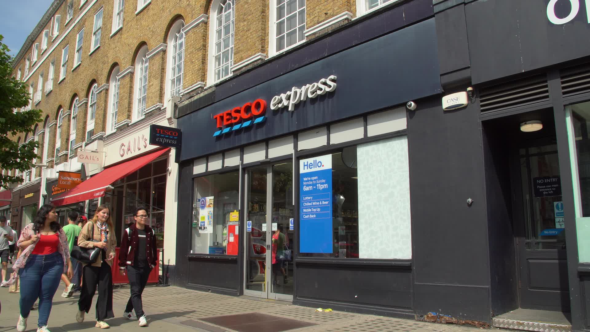 Tesco Express Storefront with Pedestrians on Sunny Day