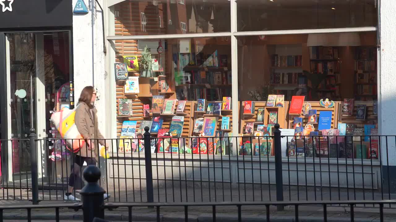 Pedestrian Passing a Bookstore Display under Sunlight