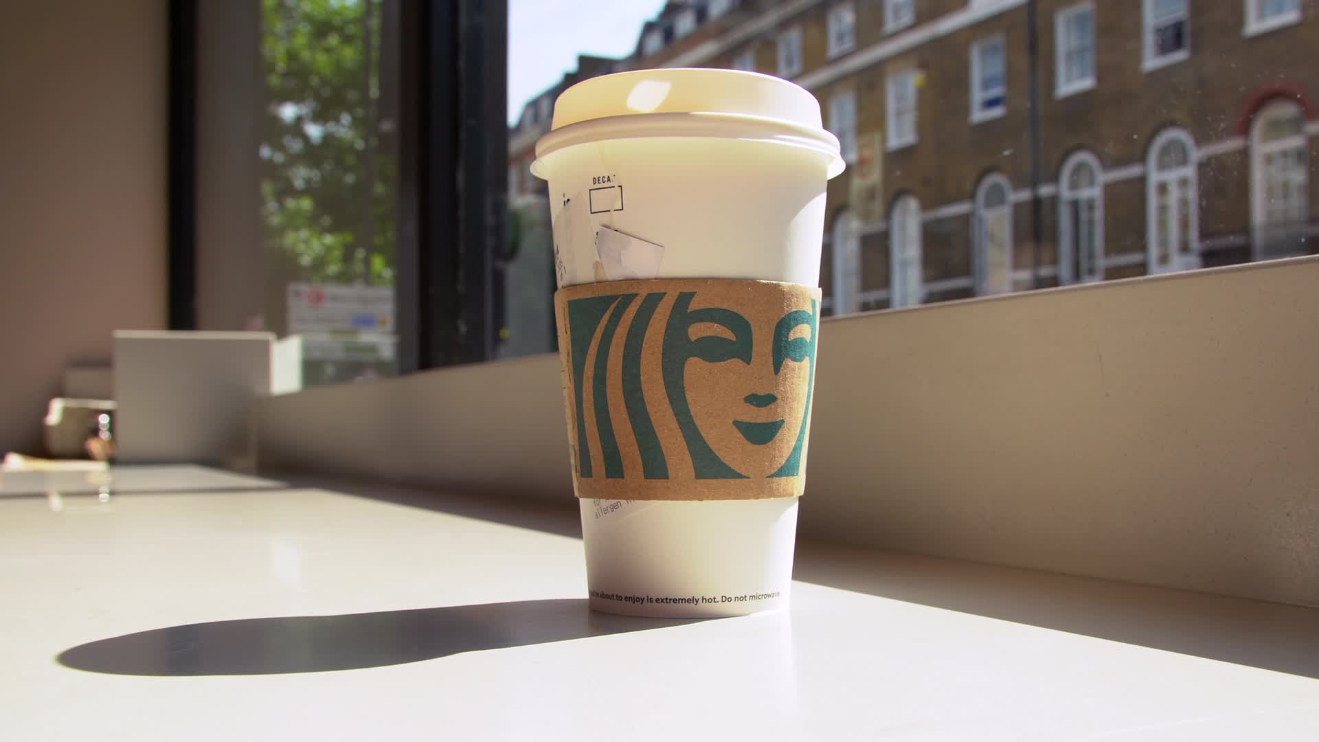 Close-Up of Starbucks Cup by Window in Sunny Cityscape